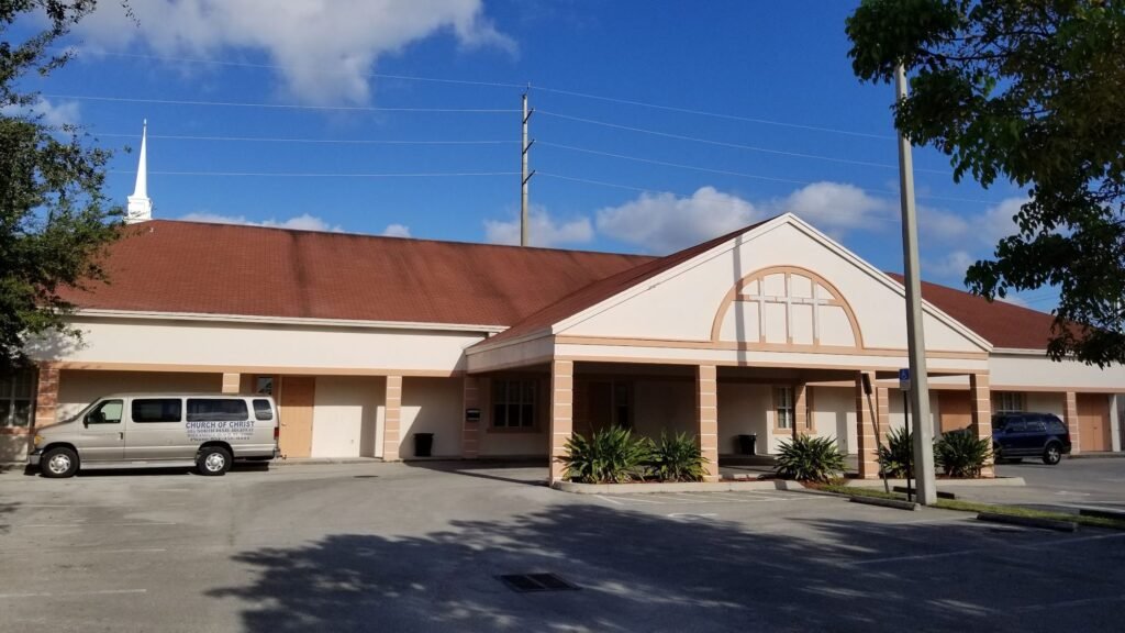 Front entrance of the Hallandale Beach Church of Christ, a peach building with a red tile roof and arched gable